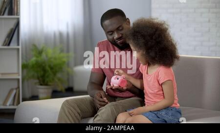 Caring father teaching child to save money, girl putting coins into piggy bank Stock Photo