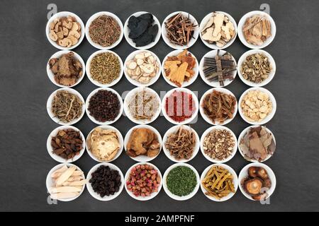 Traditional Chinese herb collection used in herbal medicine in white porcelain bowls on slate background. Stock Photo