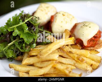 Meatballs with tomato sauce and mozzarella served with french fries and a mixed leaf salad. Stock Photo