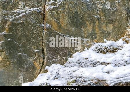 Rocky slope partially covered with snow for use as an abstract background and texture. Stock Photo