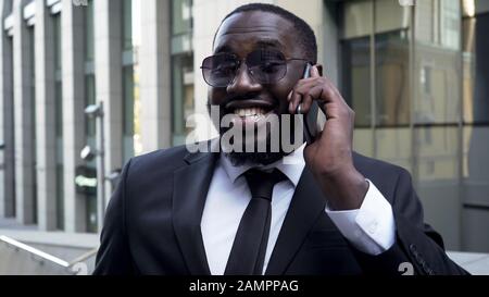 Black man in business suit talking over cellphone, smiling hearing good news Stock Photo