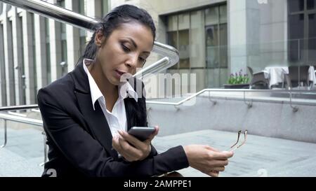 Busy woman checking e-mails on smartphone outdoors near office, lunch time Stock Photo