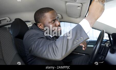 Suspicious business man looking in rear-view mirror, notices spy pursuit on road Stock Photo