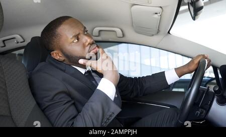 Handsome African-American businessman looking in car mirror, having doubts Stock Photo