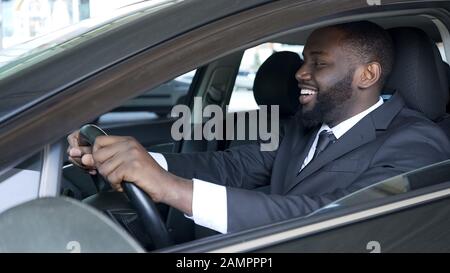 African American man sitting in expensive car satisfied and smiling, test drive Stock Photo