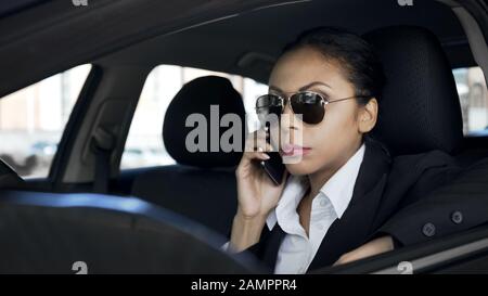 Serious woman talking on phone in car, private detective spying, police agent Stock Photo