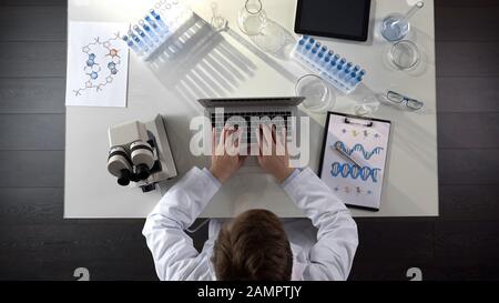 Genetics scientist conducting medical studies of DNA, typing on laptop, top view Stock Photo
