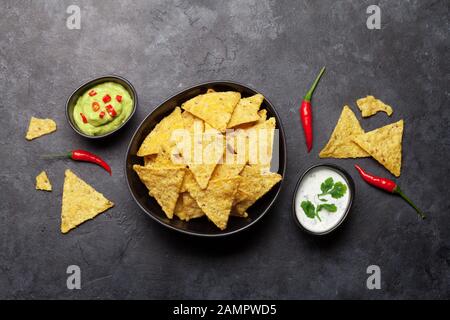 Mexican nachos chips with various sauces - guacamole and sour cream. Top view flat lay on stone table Stock Photo