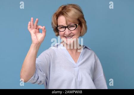 Smiling senior lady in glasses gesturing perfect sign. Teacher approving her students choice Stock Photo