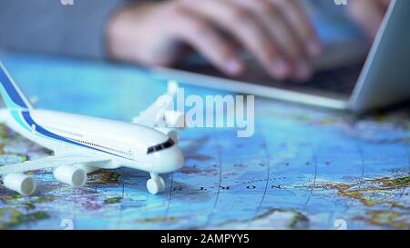 Airplane model closeup, defocused person booking flight tickets online on laptop Stock Photo