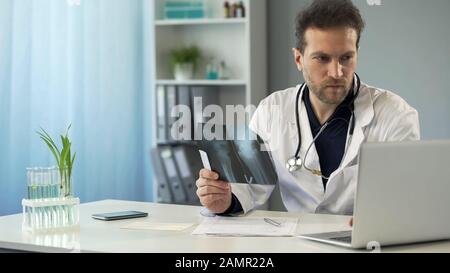 Surgeon studying x-ray of bone and making prescription in online card on laptop Stock Photo