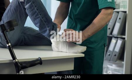 Doctor bandaging patients leg, injury treatment in rehabilitation center, health Stock Photo