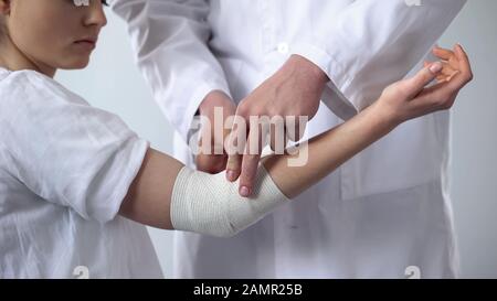 Specialist taking care of injured elbow, bandaging, first aid in trauma clinic Stock Photo