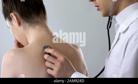 Young female coughing hard, doctor listening to her lungs, pneumonia treatment Stock Photo