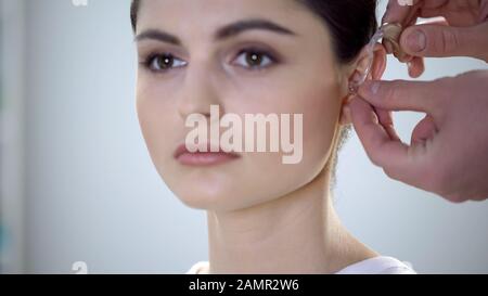 Physician putting deaf aid on young womans ear, hearing impairment treatment Stock Photo