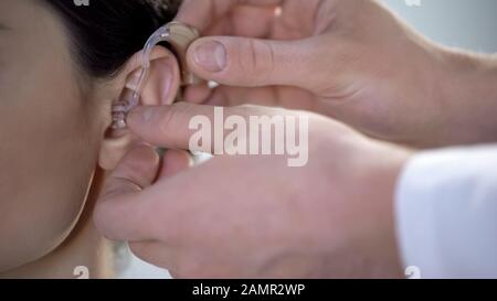 Doctor puts deaf aid on young lady ear, hearing impairment treatment, help Stock Photo