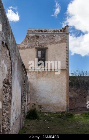 Destroyed and weathered wall of an abandoned building (kasbah) with a window.  Blue sky with white clouds. Dar Caid Hajji, Morocco.