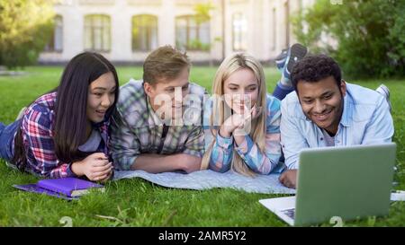 Group of multi-ethnic students relaxing on grass and watching video on laptop Stock Photo