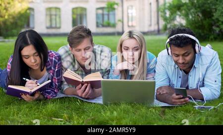 Mixed-race students lying on grass and preparing for exams, university education Stock Photo
