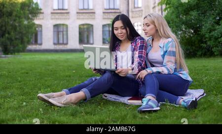Female friends watching video on laptop and discussing last student party Stock Photo