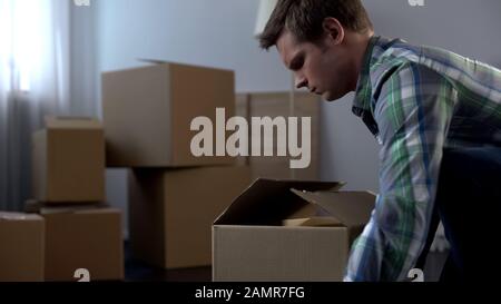 Young man packing things in cardboard boxes, moving from dormitory to own house Stock Photo