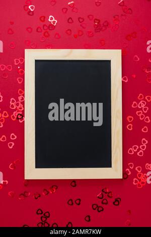 Top view of empty blackboard on red background with shiny confett. Stock Photo