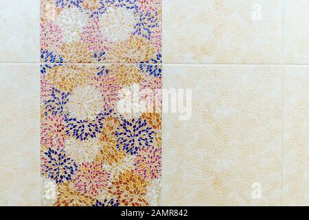 Square ceramic tiles in the form of blue, yellow, red and white leaf patterns on the wall in the bathroom. White-yellow patterns alternate with Stock Photo