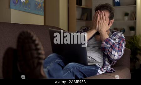 Tired adult man sitting on couch, closing face with hands, continuous job search Stock Photo
