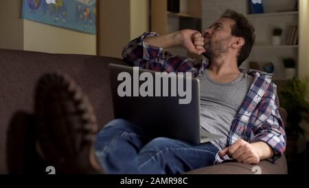 Guy sitting on sofa with laptop and thinking about online project, freelancer Stock Photo