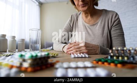 Unhealthy elderly lady suffering pain looking at pills, painkillers hypochondria Stock Photo