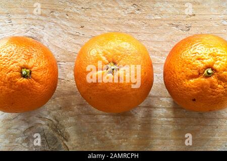 Three orange organic blood oranges in an horizontal row on weathered wooden table with copy space. Flat lay. Stock Photo