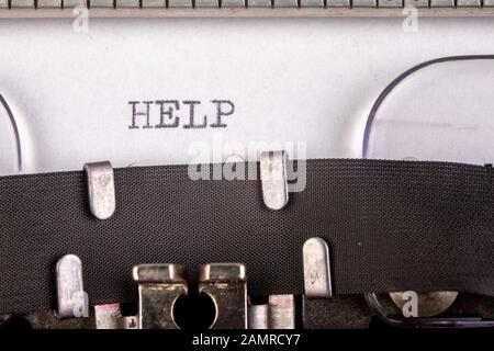 The inscription "help" on a white sheet of paper in an old typewriter. The old method of printing text. Light background. Stock Photo