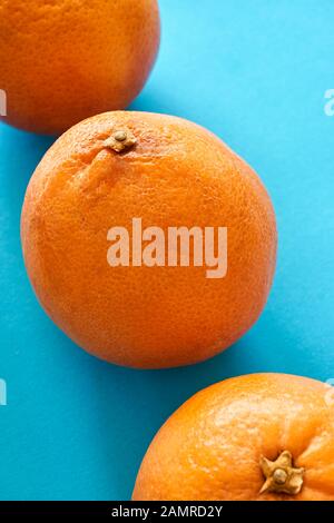 Closeup of a diagonal row of three vibrant orange blood oranges on light blue or teal background. Vertical image. Stock Photo