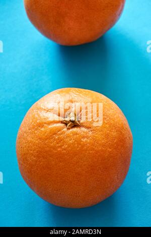 Closeup of two vibrant orange blood oranges on light blue or teal background. Vertical image. Stock Photo