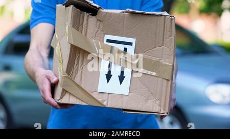 Frightened delivery worker giving broken customer parcel, shipment accident Stock Photo
