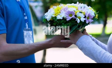 Delivery man giving bouquet to woman, easy order and delivery of flowers service Stock Photo