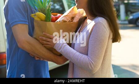 Smiling woman receiving grocery bag from delivery worker, supermarket service Stock Photo