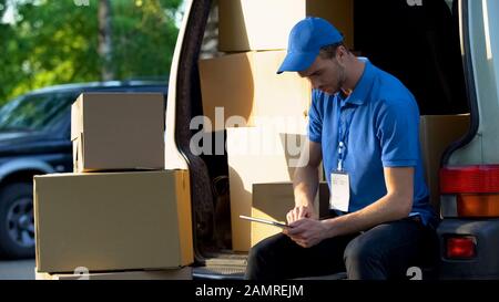 Delivery worker checking parcel amount in van, stocktaking report on tablet Stock Photo