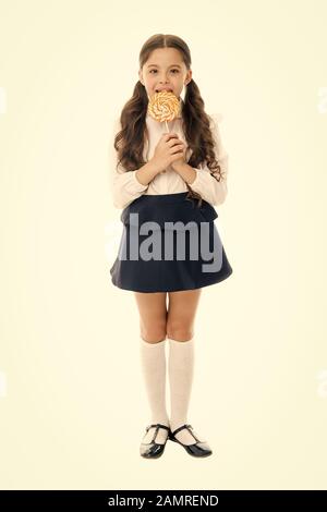 Rewarding herself with sweets. Food addictions. Girl kid eat sweet lollipop. Girl pupil school uniform like sweets lollipop candy white background. Healthy nutrition diet. Sweets reward for study. Stock Photo