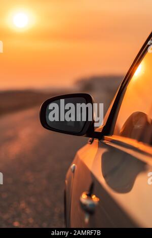 Side view mirror of car on road in autumn sunset for travel, car insurance or roadside assistance concept, selective focus Stock Photo