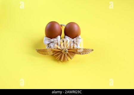 Easter holiday concept, handmade pink white gingerbread cookies in the form of a bunny on a yellow background. Gingerbread paschal rabbit with straw Stock Photo