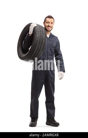 Full length portrait of a mechanic carrying a car tire and smiling at the camera isolated on white background Stock Photo