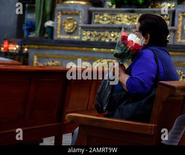 woman holding roses wrapped in plastic in St. Peter's Church in Tlaquepaque, Mexico Stock Photo