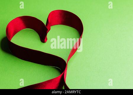 A red heart shaped ribbon on a green background can be used as a card background or Wallpaper for Valentine's Day. Stock Photo