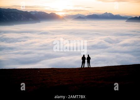 Silhouette of two women on a mountain peak at sunset looking at the view, Salzburg, Austria Stock Photo