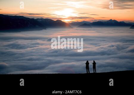 Silhouette of two women on a mountain peak at sunset looking at the view, Salzburg, Austria