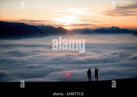 Silhouette of two women on a mountain peak at sunset looking at the view, Salzburg, Austria Stock Photo