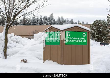 A recycle drop off bin for clothes and shoes sits in a parking lot covered in snow in an American Northwest mountain city during winter. Stock Photo