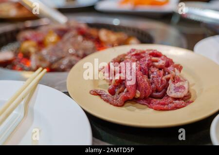 Close up view of raw beef meats on plastic plate and blur background of grilled meat on Electric Grill Griddle. Stock Photo