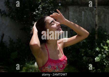 Teenage girl standing in a garden cooling off under a water sprinkler, Argentina Stock Photo